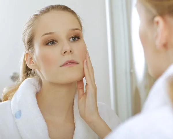 A woman is seeing her reflection in a mirror while holding her right cheek